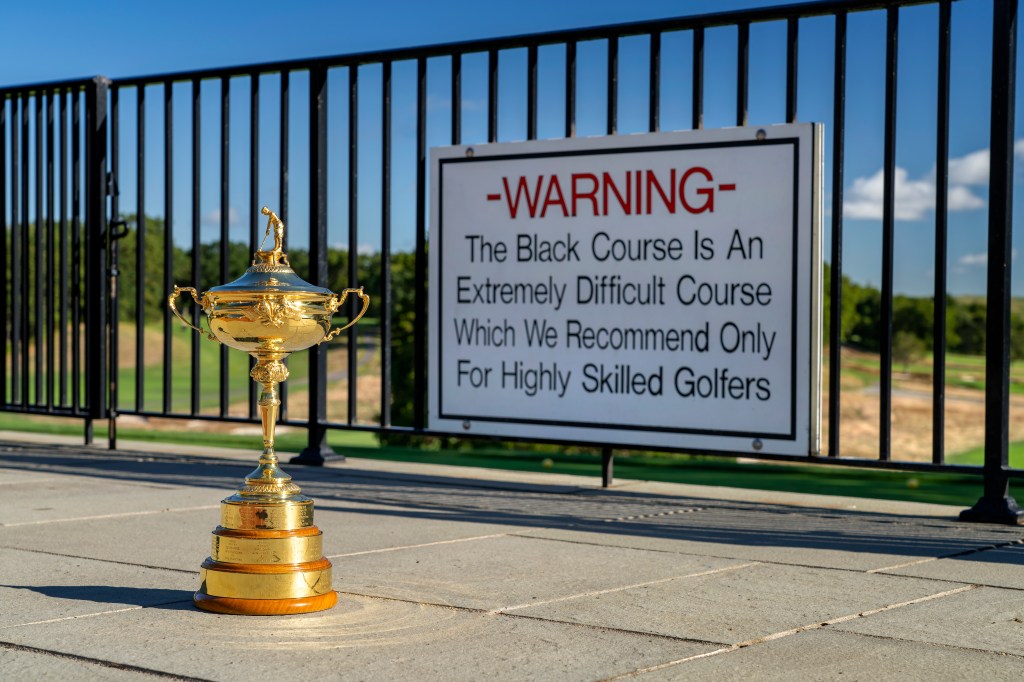 A golden trophy displayed in front of a warning sign at Bethpage State Park's Black Course, indicating it is extremely difficult and recommended for highly skilled golfers.