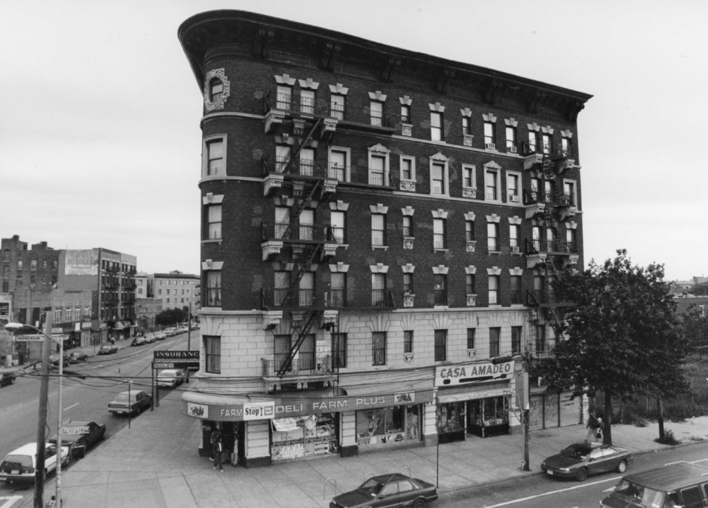 Historical black and white photograph of the Manhanset Building in the Bronx, featuring the storefront of Casa Amadeo on the ground floor, showcasing Neo-Renaissance architectural style with decorative cornices and windows.