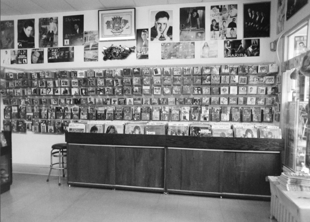Interior of Casa Amadeo, antigua Casa Hernández, showcasing a wall filled with music CDs and posters of Latin music artists, with a counter in the foreground.