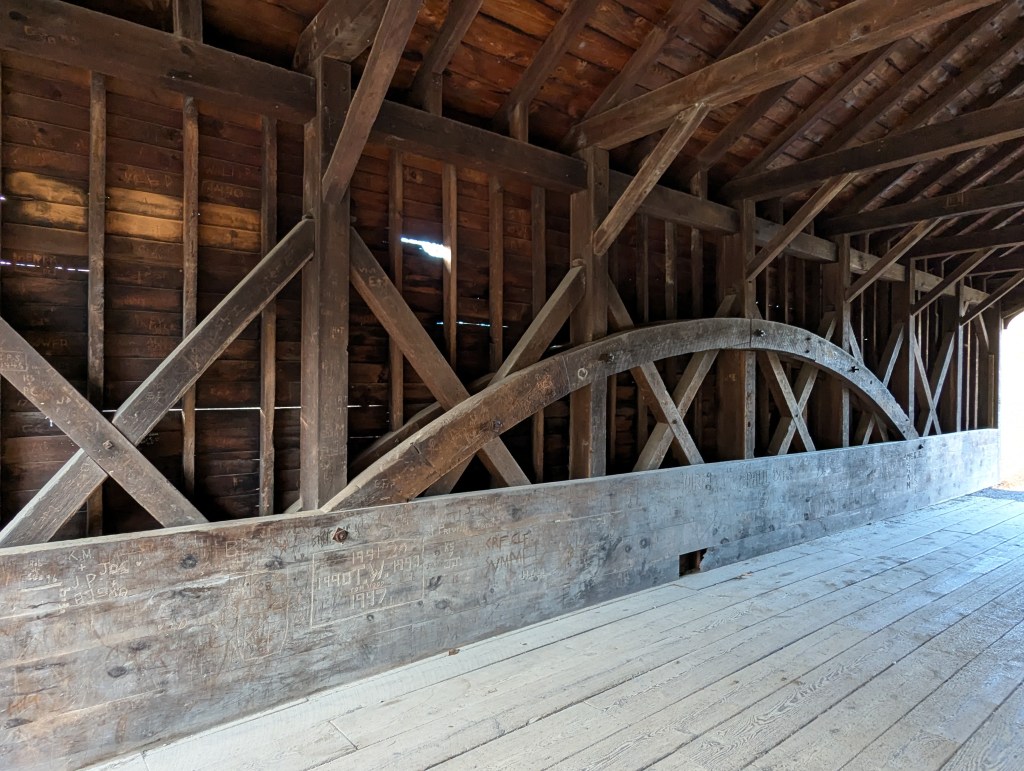 Interior view of the Hyde Hall covered bridge showcasing wooden beams, flooring, and historical carvings on the walls.