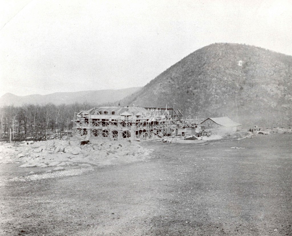 Historic black and white photograph of the construction site of a building in the Palisades region, with a mountain in the background.